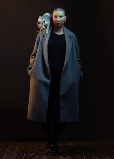 femme dans un studio photo sur un fond noir qui pose avec un chat sphynx et qui porte un pull gris mode pour un shooting photo fashion