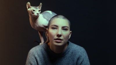 femme dans un studio photo sur un fond noir qui pose avec un chat sphynx et qui porte un pull gris mode pour un shooting photo fashion