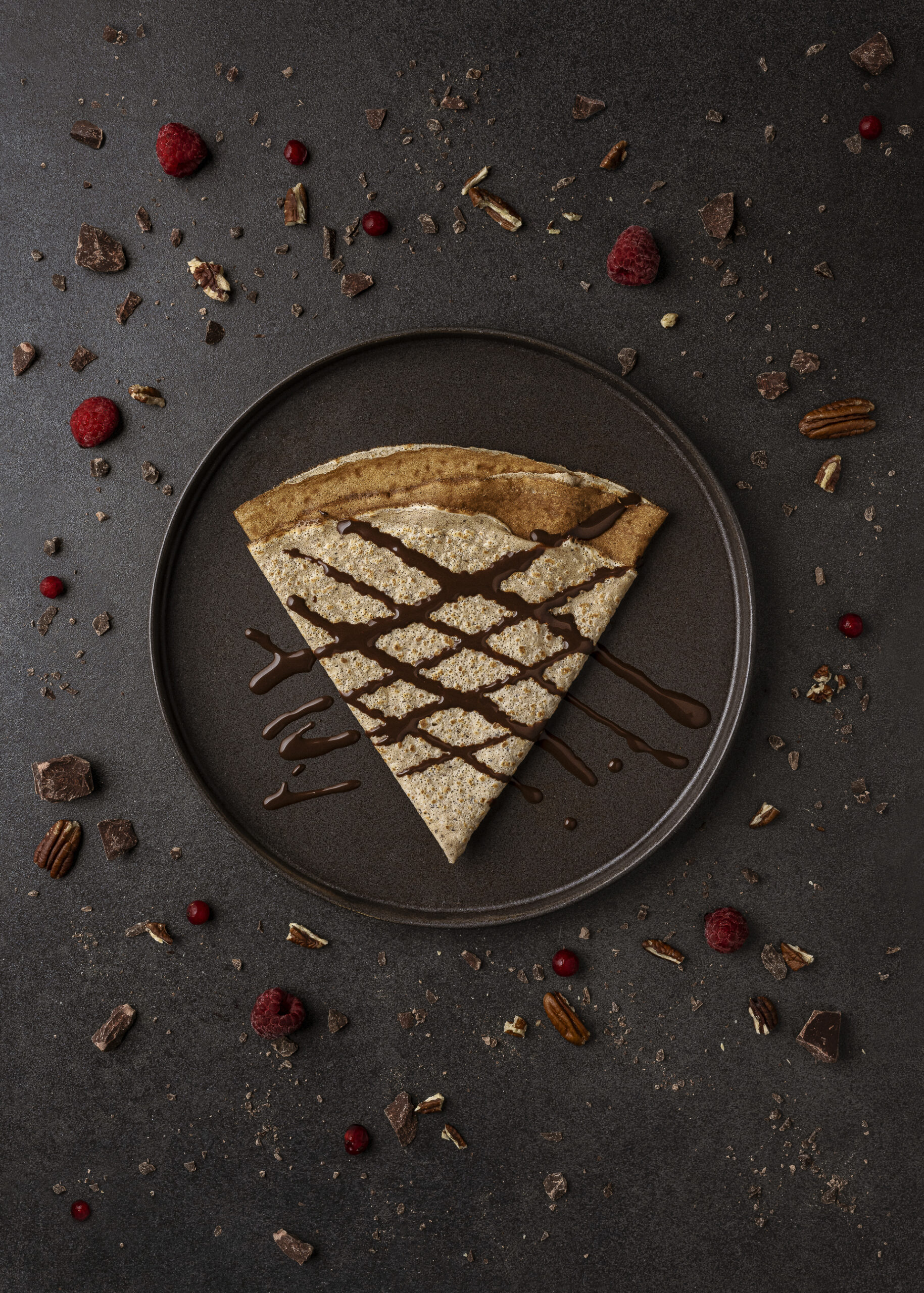 Photographie culinaire, réalisée en studio photo professionnel à Neuchâtel en Suisse. Crêpe vue de dessus sur un fonf béton noir avec des ingrédients posés tout autour de la crêpe qui viennent et apportent la création de l'image. Foodphotography shooting photo par bacchus production visuelle.